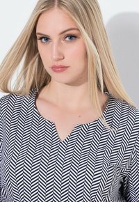 Zwart-wit chevronpatroon blouse met V-hals, zachte textuur en een relaxte pasvorm. Lichtgewicht stof met een opvallend grafisch ontwerp.