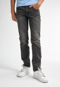 Jeans de denim oscuros ajustados con una textura desgastada; cuentan con cinco bolsillos y un cierre de botón; combinados con zapatillas blancas.