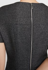 Czarna sukienka z teksturowym połyskiem, z zamkiem błyskawicznym z tyłu. Krótkie rękawy i dopasowany krój podkreślają nowoczesną sylwetkę.