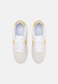 Sneakers z beżową zamszową cholewką, białymi sznurowadłami i żółtymi akcentami. Perforowana część palców i wyściółka z amortyzacją. Teksturowana podeszwa dla lepszej przyczepności.