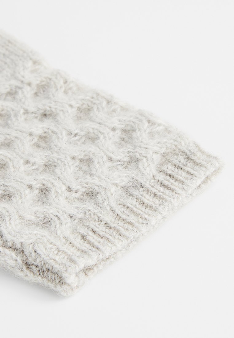 Weiche, hellgraue gestrickte Stoffhülle mit einer flauschigen Textur und einem detaillierten Zopfmuster auf weißem Hintergrund.