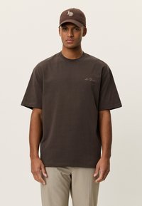 Καφέ κοντομάνικο t-shirt με στρογγυλή λαιμόκοψη και άνετη εφαρμογή, με διακριτική κεντητική λεπτομέρεια στο στήθος. Συνδυάζεται με καπέλο σε ταιριαστή καφέ απόχρωση.