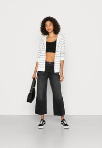 Striped white and blue zip-up hoodie, black crop top, wide-leg black jeans, black bag, and black and white sneakers.