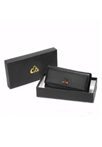 Portafoglio in pelle nera testurizzata con un emblema decorativo a forma di ape, adagiato in una scatola nera con logo dorato sul coperchio.