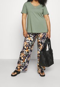 Oliivinvihreä lyhythihainen t-paita, kukkakuvioiset tummansiniset leveälahkeiset housut, musta punottu olkalaukku ja mustat tasapohjaiset sandaalit.