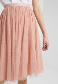 Gonna midi rosa pallido realizzata in tulle sovrapposto con motivo a pois, dotata di una vita aderente e delicate rifiniture in pizzo all'orlo.