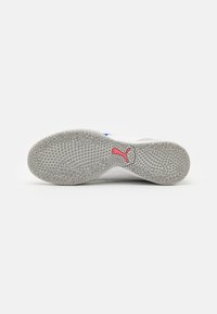 Suela de zapatilla deportiva blanca con un patrón de agarre circular, material de goma gris y un pequeño logo rojo entre el talón y el arco.