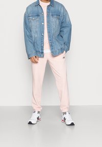 Giubbotto di jeans in azzurro chiaro con vestibilità rilassata, abbinato a pantaloni tuta rosa e scarpe da ginnastica bianche con un accento nero.
