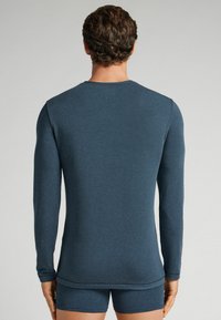 Langärmliges Hemd aus dunkelblauem strukturiertem Stoff mit Rundhalsausschnitt und taillierter Silhouette, kombiniert mit passenden Shorts.