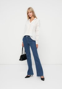White, eyelet blouse with a V-neck and long sleeves, paired with blue striped flared jeans, and black pointed-toe shoes. Black handbag.