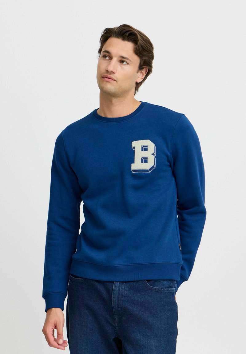 Plava dukserica od pamuka, s okruglim izrezom i rebrastim manžetama. Na prsima je ušivena velika, stilizirana bež sl letters "B".