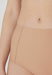 Světlé hnědé vysoké spodní prádlo s hladkým materiálem, bezešvým designem a jemným prošíváním podél okrajů.