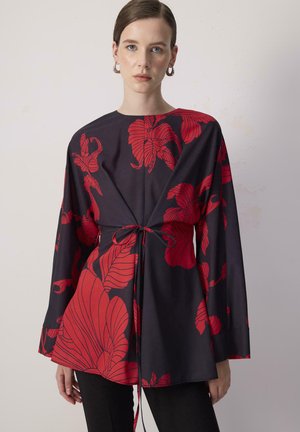 Zwarte blouse met rode bloemenpatroon, lange mouwen, ronde halslijn en strikdetail in de taille. Glad materiaal met een ontspannen pasvorm.