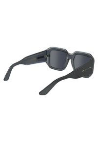 Occhiali da sole grigi con una montatura in plastica angolare e lenti scure. Le caratteristiche includono un accento metallico sul lato e un design della cerniera robusto.