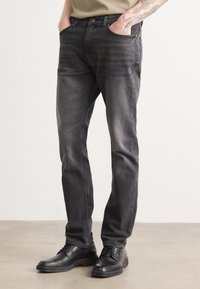 Black denim jeans with a slim fit, featuring five pockets and subtle fading. Worn with black dress shoes.