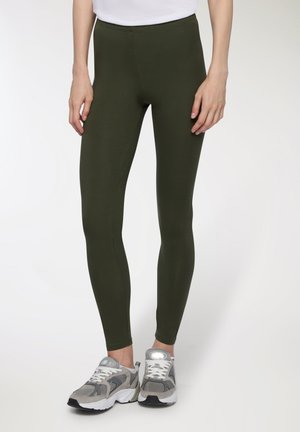 Leggings verde oliva realizzati in un tessuto elasticizzato, caratterizzati da una vita alta e un design liscio e senza cuciture. Abbinate a scarpe da ginnastica grigie.
