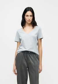 Φωτεινό γκρι t-shirt με V-λαιμό, κοντά μανίκια, κατασκευασμένο από απαλό βαμβάκι. Συνδυάζεται με σκούρο γκρι φόρμα με ρυθμιζόμενο κορδόνι στη μέση.