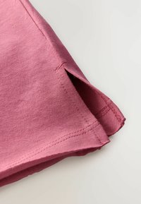Bomulds T-shirt ærme i støvet rosa farve med en sidesøm split, rengjort syning og blød tekstur.