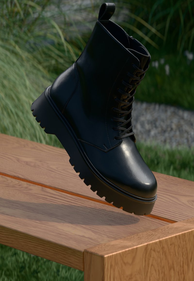 Juodas odinis kulkšnių botas su tekstūruota paviršiumi, raišteliais priekyje ir stambiu, grublėtu padu. Pateiktas ant medinės plokštės su žolės fonu.