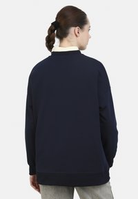 Sudadera azul marino con textura suave, corte oversized y puños acanalados. Presenta un escote redondo y un diseño de hombros caídos.