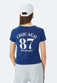 Laivastonsininen lyhythihainen t-paita, jossa on valkoinen teksti "CHICAGO 87" ja "Yhdysvallat". Kontrastivärinen vivaus kaula-aukossa ja hihoissa.
