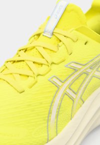 Helles gelbes Sport Schuhwerk mit strukturiertem Obermaterial, flachen Schnürsenkeln und reflektierenden Akzenten. Verfügt über ein leichtes Design und das Asics-Logo.