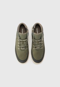 Pair of olive green Timberland sneakers with beige soles, reflective laces, and side zippers on a white background.