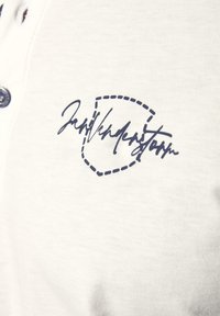 Cremfarbener Poloshirt mit einem dunkelblauen gestickten Signaturlogo und einem Wendenkragen mit dunklen Knöpfen.