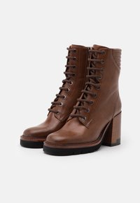 Bottes chevilles en cuir marron avec des talons épais et carrés, des bouts ronds et des lacets. Comprend des accents texturés et des œillets en métal ronds pour les lacets.
