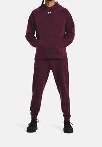 Completo felpa e pantaloni jogger color bordeaux in morbido tessuto testurizzato con cappuccio regolabile, caratterizzato da un logo frontale e polsini in elastico. Scarpe da ginnastica nere completano l'outfit.