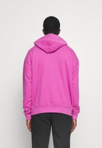 Sweat à capuche rose avec une coupe décontractée, des poignets et un ourlet côtelés. Doté d'une poche kangourou et d'une texture de tissu douce.