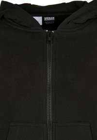 Juodas zip-up džemperis, pagamintas iš tekstūruoto audinio, su priekyje esančiu užtrauktuku ir dviem priekinėm kišenėm. Nėra matomų raštų ar detalių.