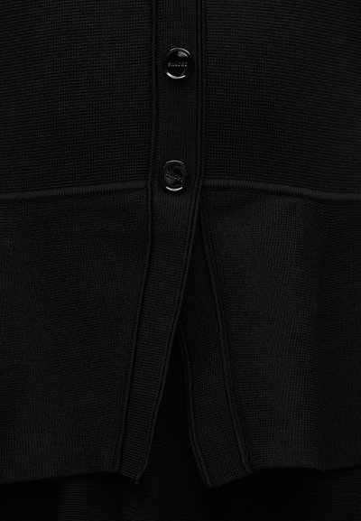 Κοντινή λήψη μαύρου υφάσματος με υφή και δύο γυαλιστερές μαύρες κουμπότρυπες τοποθετημένες κάθετα σε άνοιγμα πλεκτού ενδύματος.