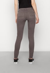 Jeans ajustados grises de cintura alta, con bolsillos traseros que presentan costuras sutiles, combinados con zapatillas negras. Textura suave y diseño ceñido.