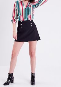 Chemise à rayures boutonnée dans les tons bleu sarcelle, rouge et jaune avec deux poches avant, associée à une jupe trapèze noire ornée de boutons argentés.