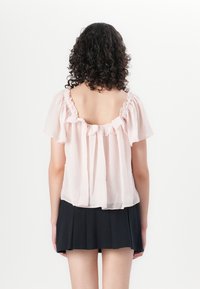 Blusa rosa trasparente con maniche corte arricciate e schiena scoperta, abbinata a una gonna nera plissettata. Tessuto morbido e leggero e design fluido.
