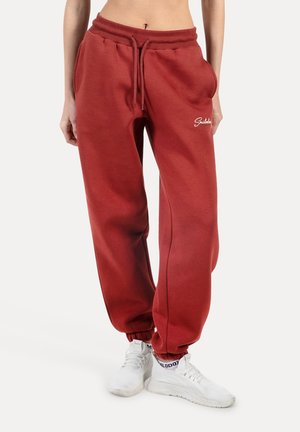 Czerwone dresy wykonane z miękkiego materiału, z elastycznym paskiem w talii ze sznurkiem i mankietami na końcach nogawek. Haftowane logo na udzie.