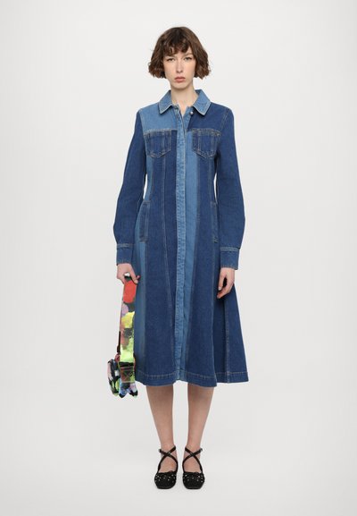 Denim obleka z gumbasto sprednjo stranjo, dolgimi rokavi in barvno blokiranim dizajnom v temno in svetlo modri. Ima dve žepni pokriti na prsih in širšo spodnji del.