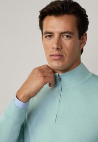 Helles blaues Zip-Hoodie mit hohem Kragen und gerippten Bündchen. Verfügt über einen gestreiften Akzent am inneren Kragen. Glatte Textur.