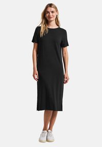 Robe noire mi-longue en tissu doux, présentant un col rond et des manches courtes, associée à des baskets blanches pour le contraste.