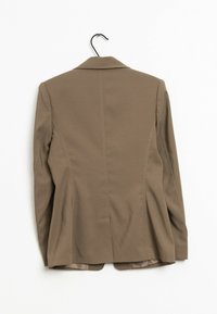 Ruskea räätälöity bleiseri, jossa on istuva muotoilu, yksittäinen takaventti ja kaarevat läpät. Sujuva kangas, jossa on hienovarainen tekstuuri. Roikkuu koukussa.