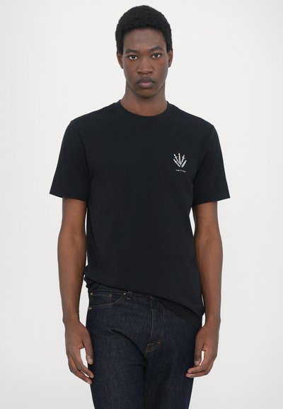 T-shirt en coton noir à manches courtes, col rond, et design brodé d'épées sur le côté gauche de la poitrine. Porté avec un jean bleu foncé.
