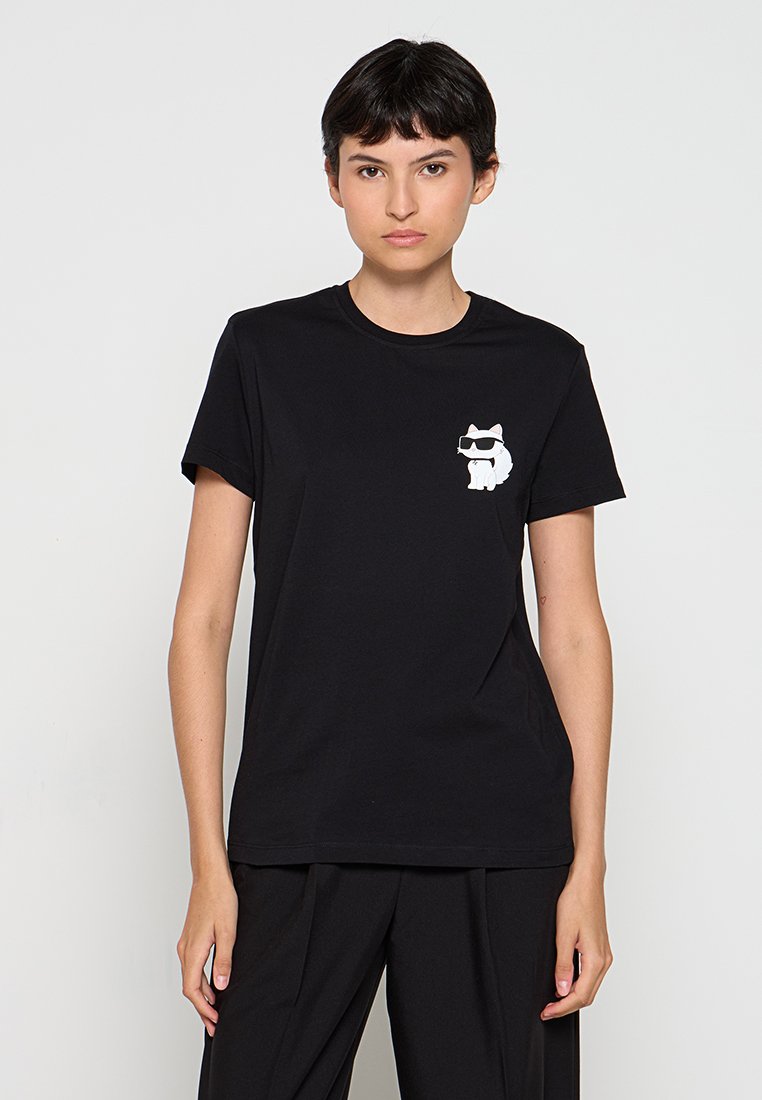 Young woman with short dark hair wearing a black T-shirt featuring a small white cat with sunglasses graphic on the chest.