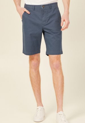 Shorts bleu marine avec un devant plat, des poches latérales et une fermeture à bouton. Fabriqués en tissu de coton, ils présentent une texture lisse et une coupe ajustée.