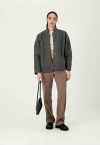 Gray fleece jacket with a relaxed fit, snap button closure, paired with beige trousers and black shoes. Holding a black handbag.
