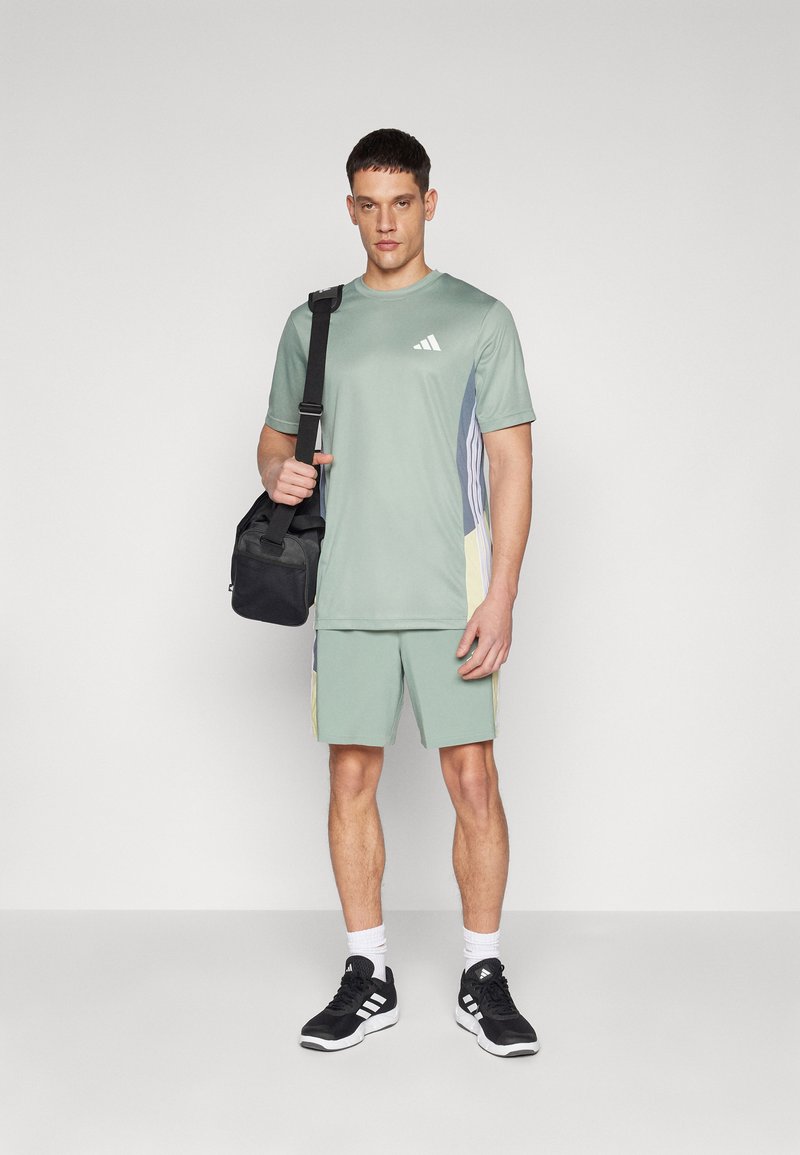 Conjunto atlético que comprende una camiseta verde claro con acentos laterales y pantalones cortos a juego. Unas zapatillas negras y un pequeño bolso negro completan el look.