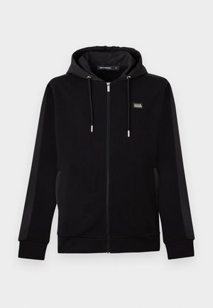 Sweat à capuche noir zippé avec cordons, poches latérales et un petit patch logo rectangulaire sur la poitrine gauche.