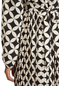 Černobílá látka se vzorem květinové geometrie. Šaty mají sklady a pás pro tvarování. Texturovaný, lehký materiál.