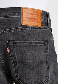 Jeans de mezclilla oscura con una etiqueta de cuero con un logo en relieve en la cinturilla trasera, costuras en el bolsillo trasero en un patrón clásico y una etiqueta roja.