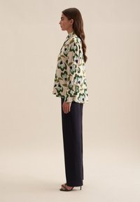 Blusa floreale color crema, con motivi di fiori verdi e blu, abbinata a pantaloni scuri e sartoriali e sandali neri con tacco.